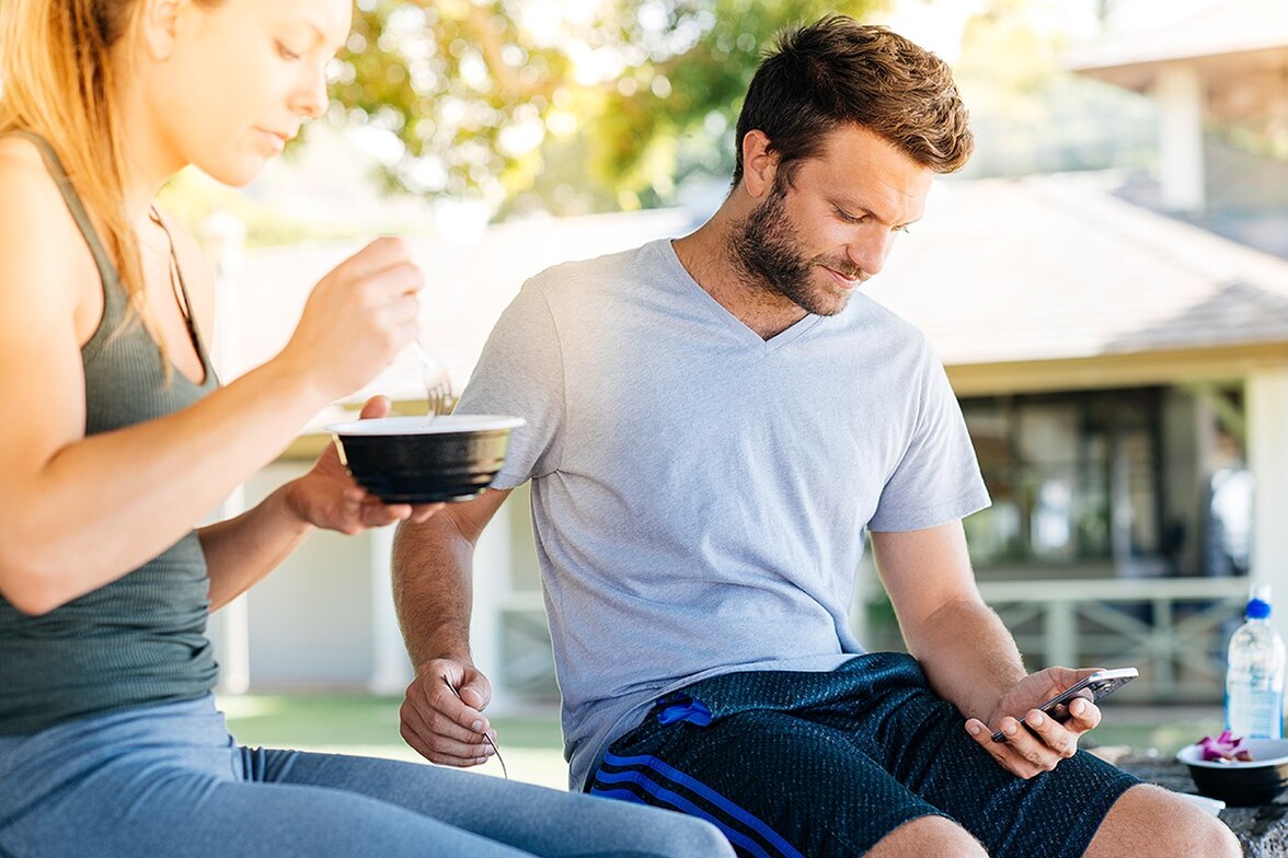 Pareja, él con celular en mano y ella con comida